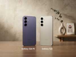 Deux smartphones Samsung Galaxy S26 FE et S26 posés sur une table en bois devant un mur texturé.