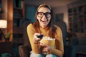 Femme à lunettes avec télécommande et pop corn, prête à streamer les séries de l'été
