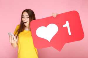 Fille avec smartphone tient un coeur "Like", car le Redmi Note 13 est bien noté et pas cher sur Cdiscount