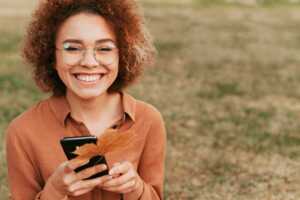 Femme aux couleurs d'automne avec smartphone sourit, ravie de ses giga en plus sur les forfaits mobile de Syma