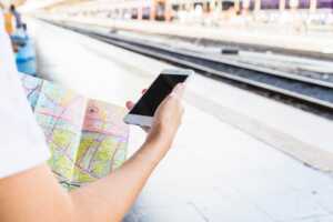 Voyageur avec smartphone et carte routière devant quai du train, car forfait Summer Edition de B&You