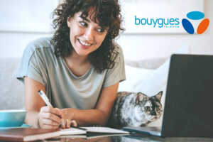 Femme travaille devant PC portable avec son chat et logo de Bouygues Telecom, ravie de sa Bbox Rentrée à 26.99€