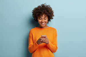 Femme en pull orange avec smartphone sourit de plaisir car forfait mobile pas cher sur le réseau d'Orange
