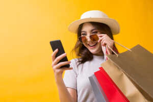 Fille au chapeau soulève lunettes de soleil pour regarder en souriant son smartphone, obtenu en vente flash chez Bouygues Telecom