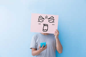 Homme avec smartphone tient carton avec dessin de visage pas content, car Sosh augmente d'1€ le prix de son forfait star