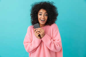 Femme à pull rose serre smartphone dans ses mains, ravie de l'iPhone 16 moins cher avec un forfait mobile de RED by SFR