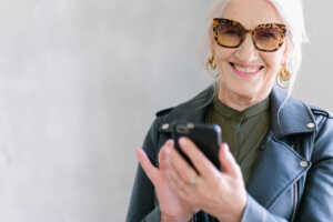 Femme à lunettes avec smartphone sourit, ravie de son nouveau forfait mobile YouPrice "Le Loop"
