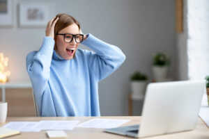 Femme devant PC du bureau, mains sur la tête et bouche bée de joie et surprise devant les nouvelles Box pas chères