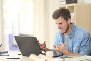 Homme énervé devant son ordinateur, car son Wi-Fi est lent à cause de la connexion d'un voisin