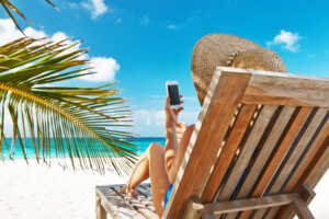 Femme dans transat à la plage avec smartphone, ravie de son forfait international de Syma