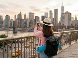 Une femme avec un sac à dos et un tapis de yoga prend en photo la skyline de New York depuis un pont grâce à un forfait Voyage ou une eSIM Voyage