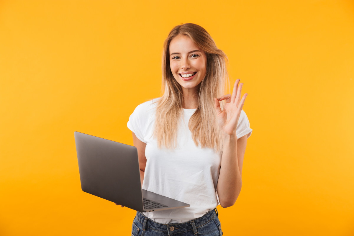 Femme avec PC portable sur fond orange fait signe que tout va bien et sourit, ravie de sa REB Box à 20€