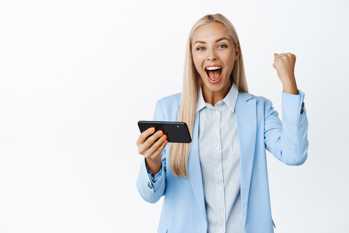 Fille avec smartphone lève le poing en signe de victoire et sourit car Syma baisse tous ses prix !