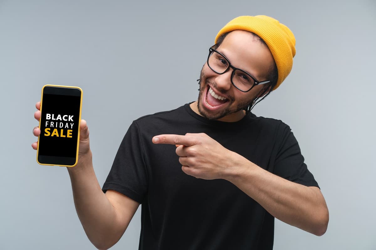 Homme à bonnet jaune montre fièrement son smartphone avec logo "Black Friday", ravie de ses 120 Go en 5G à moins de 7€ grâce à Lebara