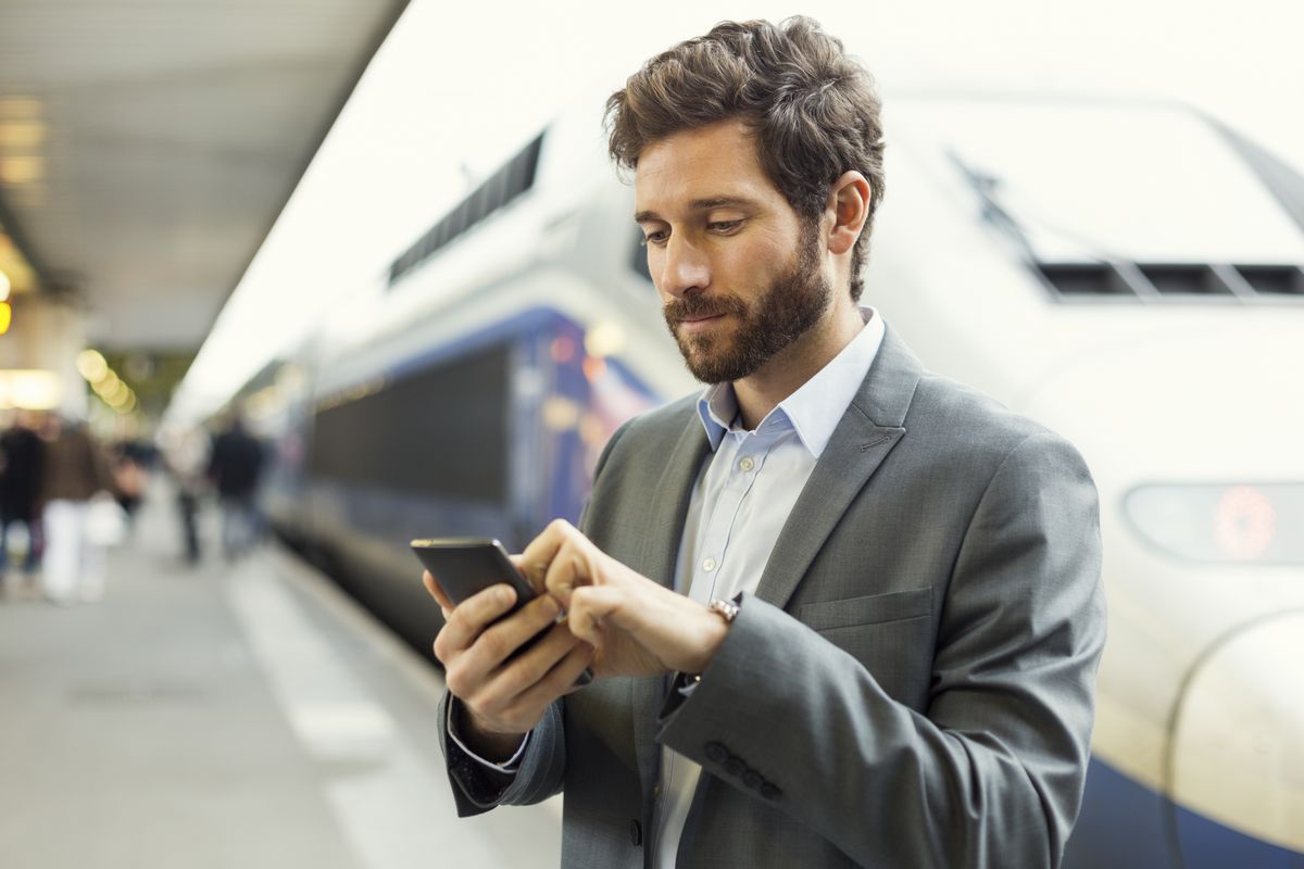 Un commercial regarde son smartphone sur le quai d'une gare TGV