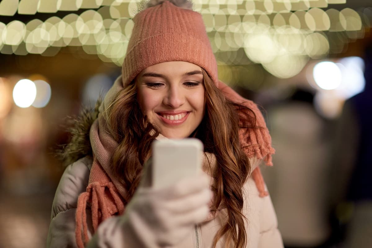Femme à bonnet sourit à son Galaxy S23 FE, en super promo chez Rakuten