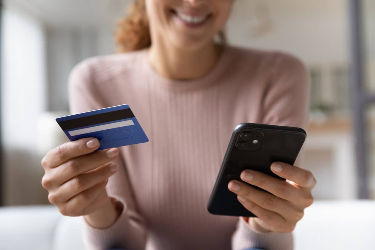 Femme avec smartphone et carte bancaire dans les mains sourit devant les forfaits de Cdiscount Mobile, bradés à moins de 10€