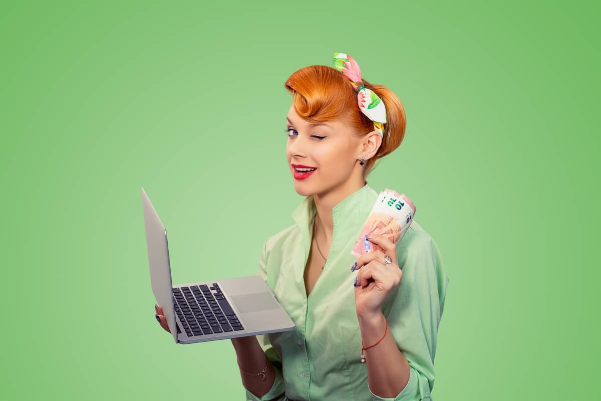 Femme rousse sur fond vert, avec un PC et des billets dans les mains, fait un clin d'oeil entendu car des mois gratuits d'abonnement avec Livebox et RED Box