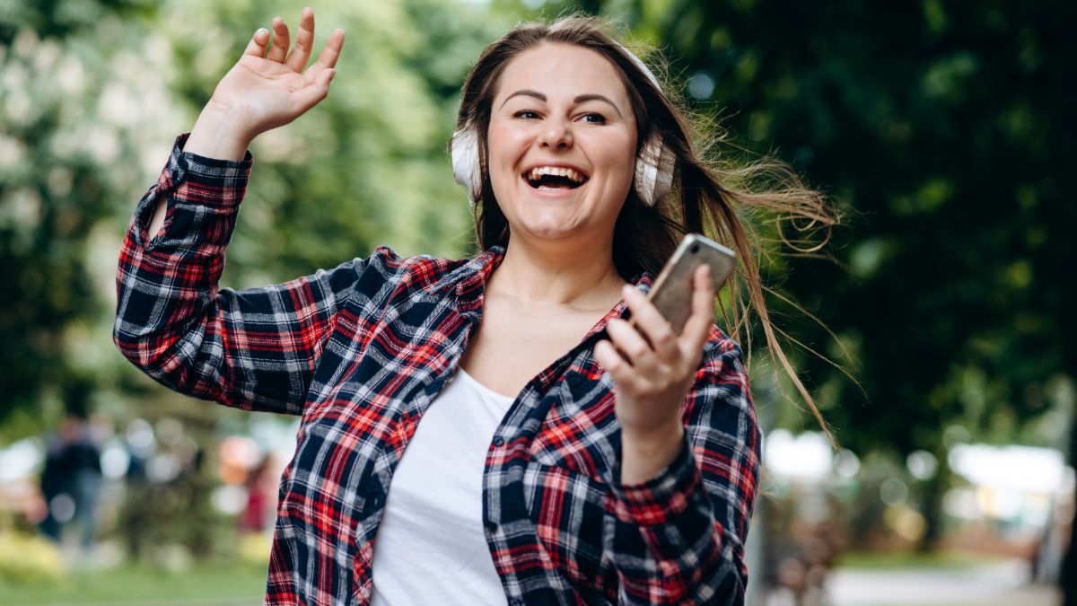 Femme dehors avec casque et smartphone sourit, ravie des 215Go de 5G de La Poste Mobile, toujours à moins de 11€ même après la fin des French Days