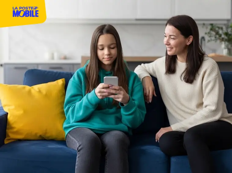 Une adolescente utilise un smartphone sur un canapé bleu à côté de sa mère.