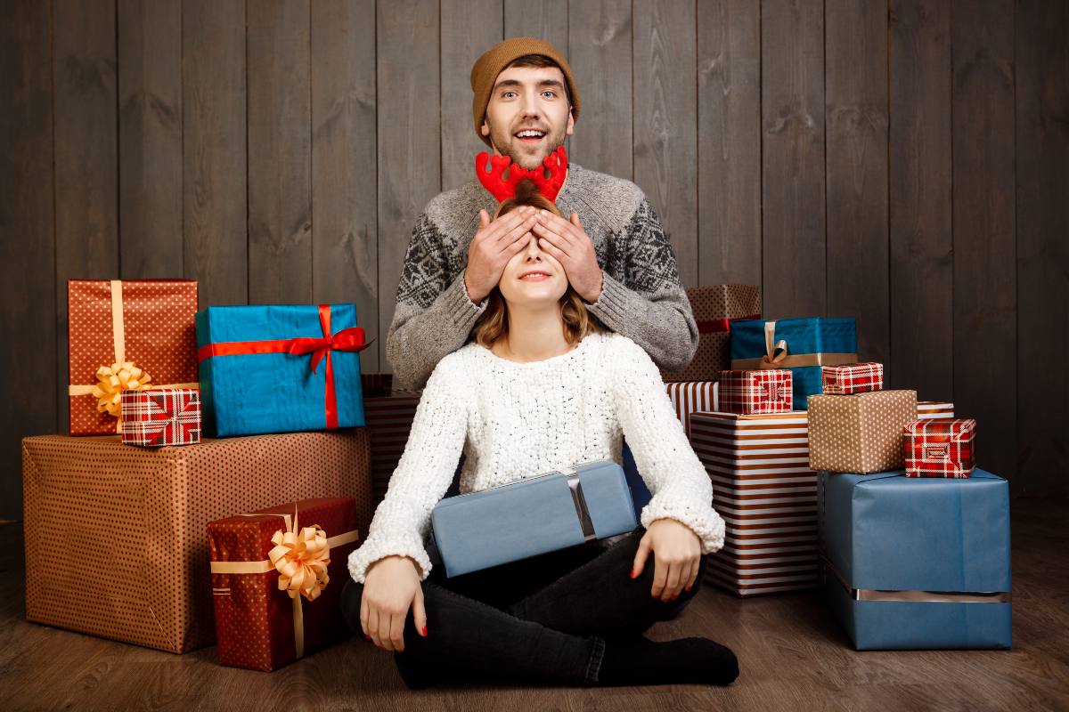 Homme cache les yeux de sa femme sur fond de cadeaux, car smartphones à petits prix et accessoires offerts chez Bouygues Telecom pour Noël, si combo avec forfait de 130 Go et plus
