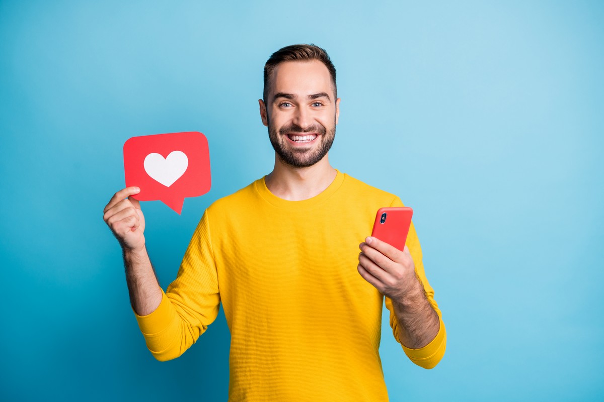 Homme en t-shirt jaune avec smartphone dans la main et coeur like, ravi de son Galaxy A16 à moins de 130€ avec un forfait 4G pas cher
