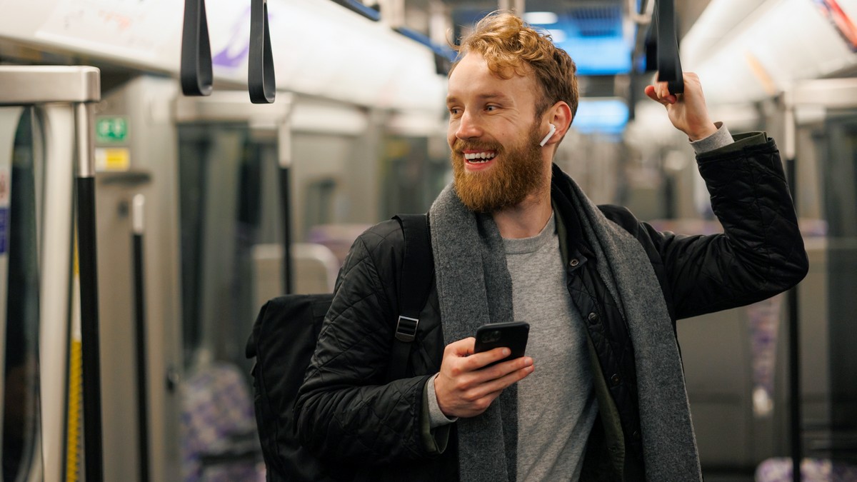 Homme dans le métro avec smartphone et écouteurs sourit, ravi de ses 200 Go de 5G Orange à moins de 10€