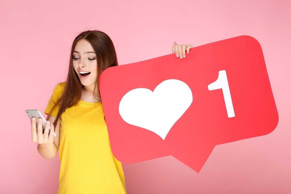Fille avec smartphone tient un coeur "Like", car le Redmi Note 13 est bien noté et pas cher sur Cdiscount