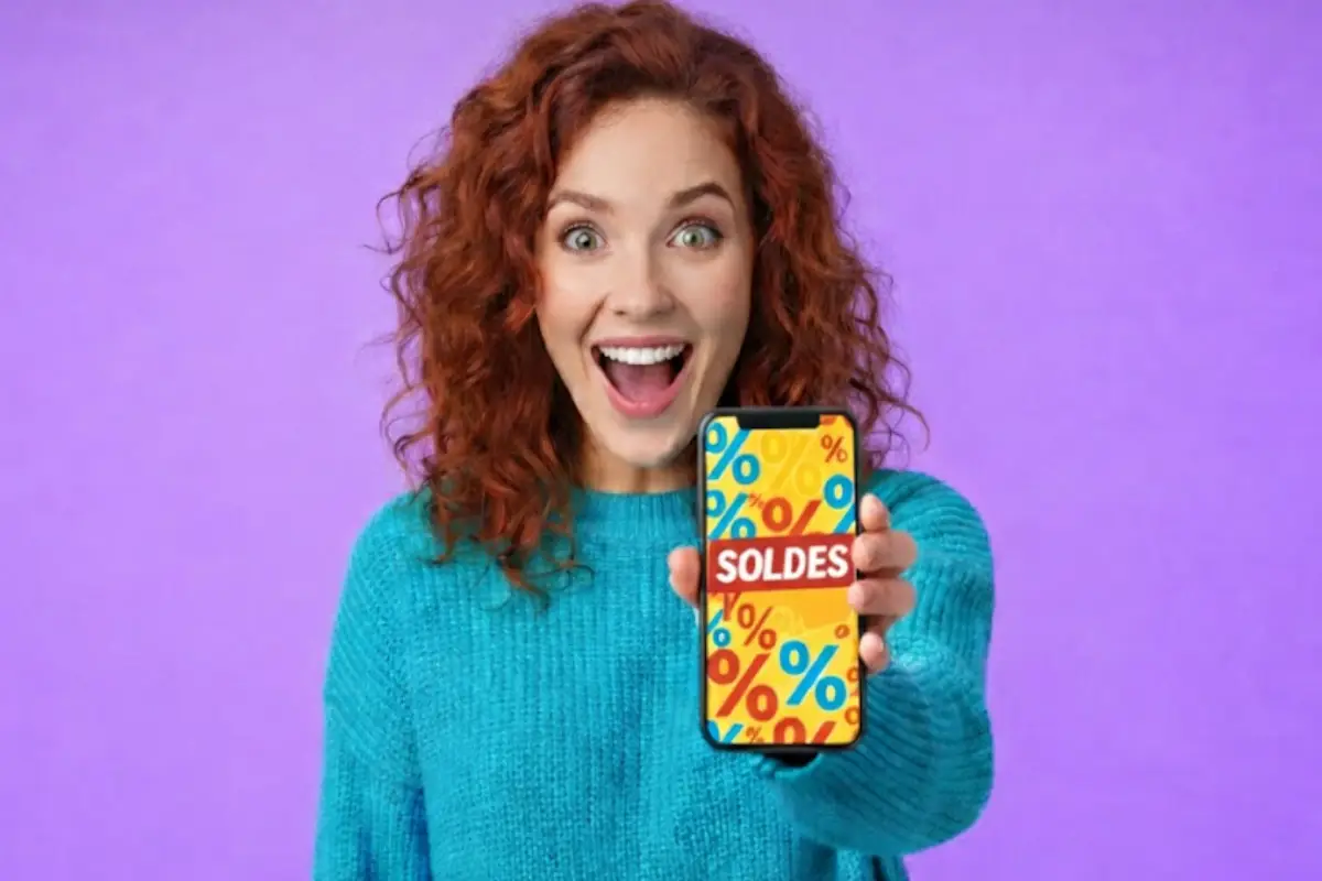 Femme montre son smartphone inscrit "Soldes" avec un grand sourire, ravie de ces 80 Go de 5G à moins de 5€ chez B&YOU