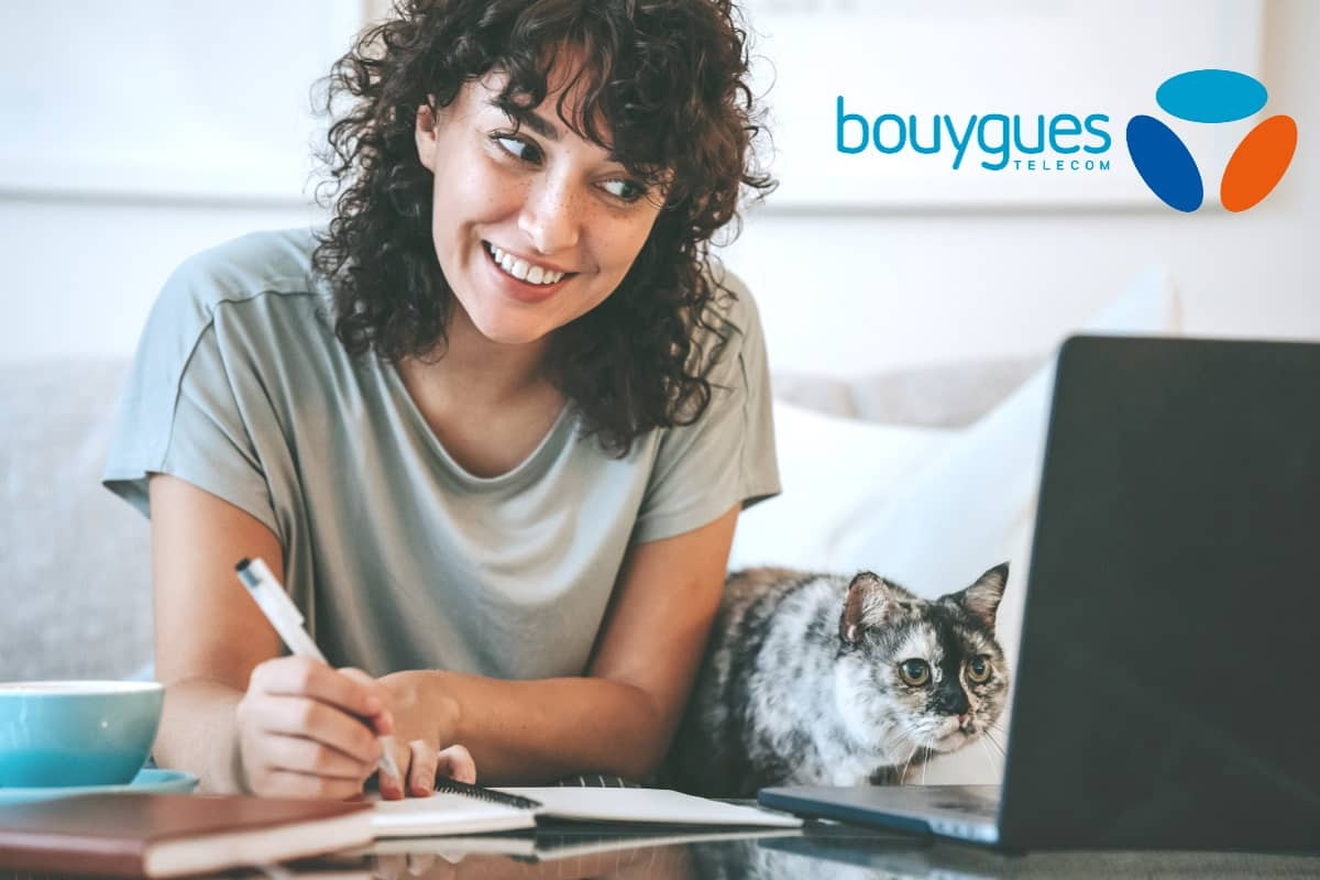 Femme travaille devant PC portable avec son chat et logo de Bouygues Telecom, ravie de sa Bbox Rentrée à 26.99€