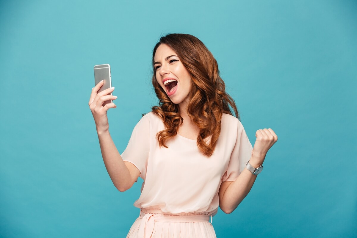 Femme sur fond bleu regarde son smartphone, très heureuse de son forfait moins cher qu'un abonnement à Netflix