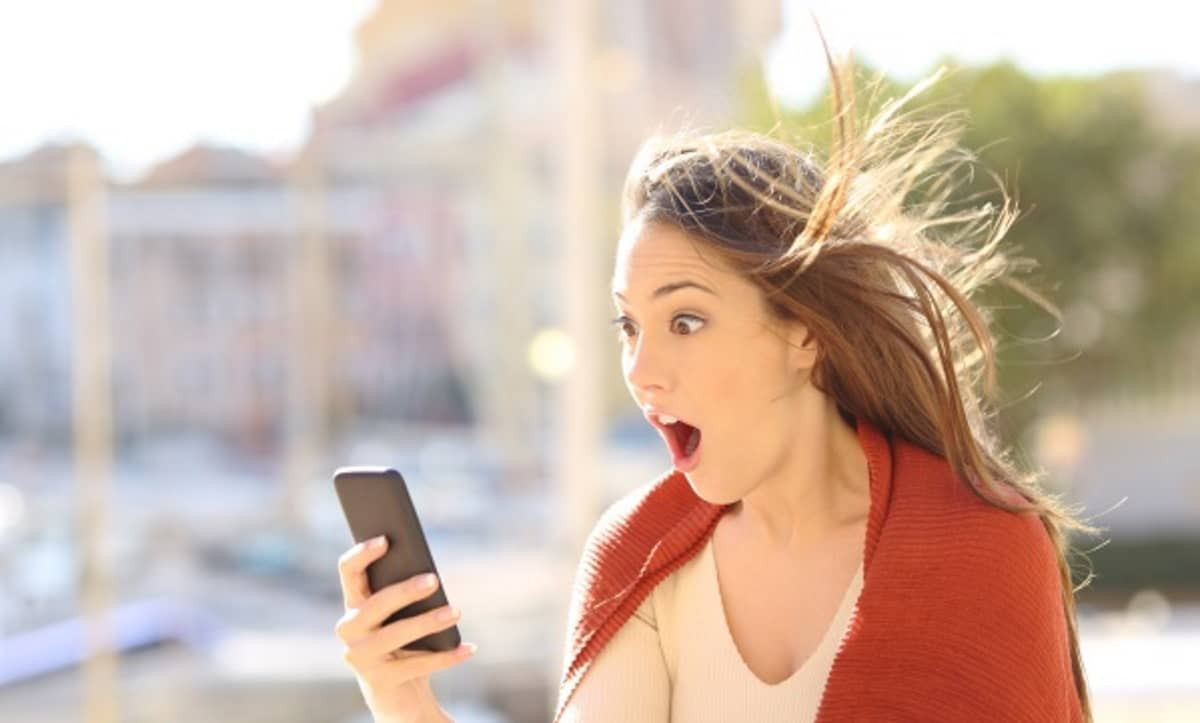 Fille avec smartphone bouche bée et cheveux ébouriffés de surprise devant le nouveau forfait mobile surpuissant de Lebara