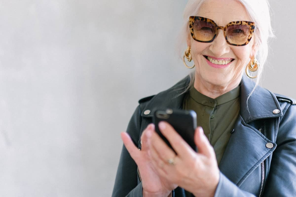 Femme à lunettes avec smartphone sourit, ravie de son nouveau forfait mobile YouPrice "Le Loop"