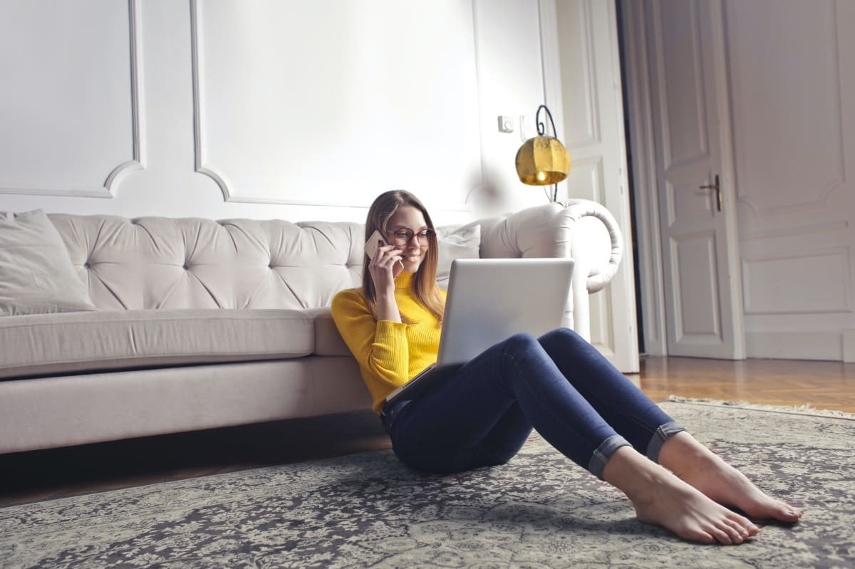 Fille dans son salon avec PC et smartphone, sourit car seulement 30€ en rassemblant ses abonnements fixe et mobile chez Bouygues Telecom