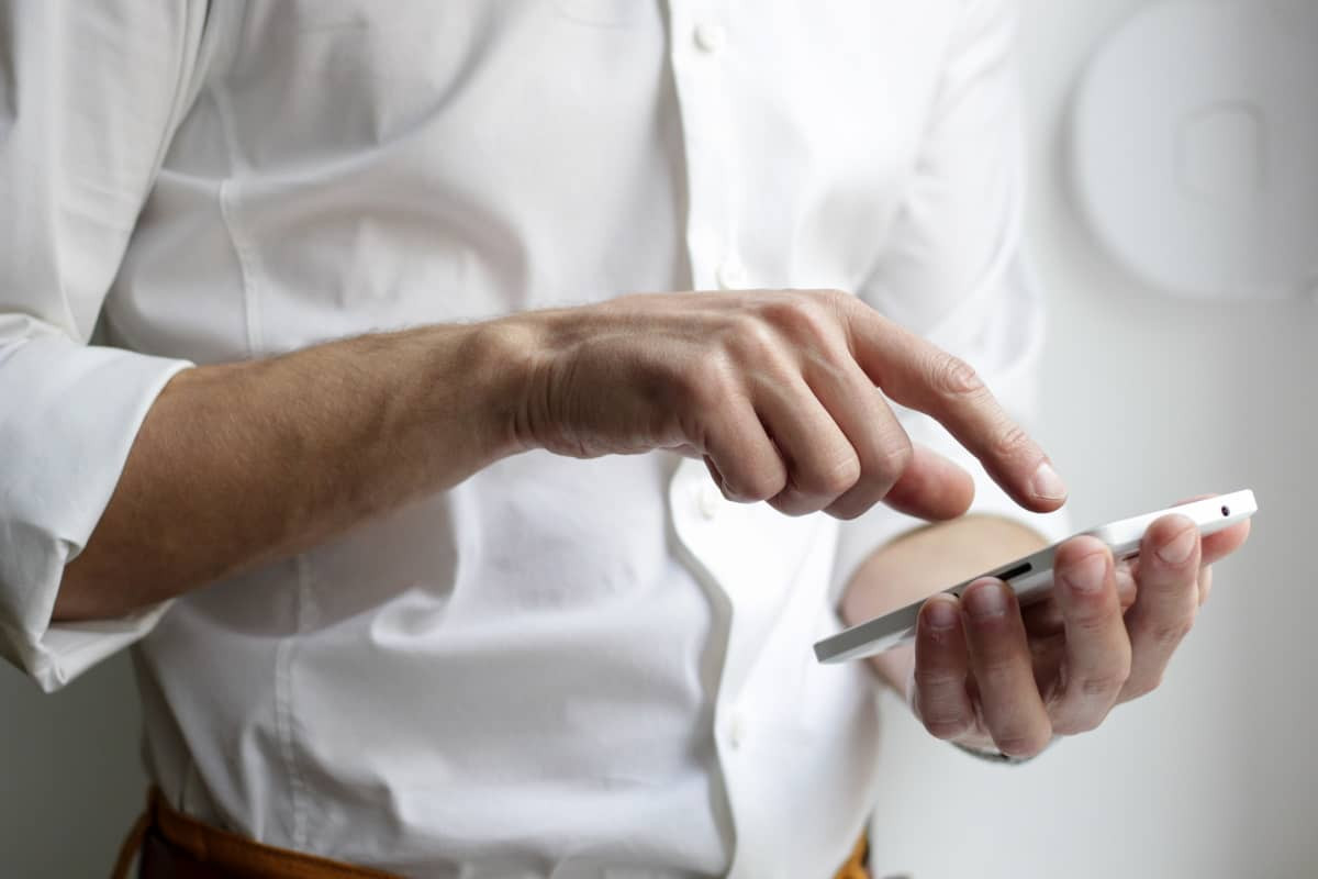 Homme en chemise blanche pianote sur son smartphone grâce aux 100 Go en 5G à moins de 8€ chez RED by SFR