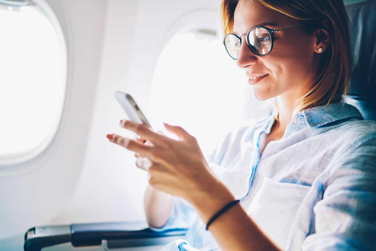 Femme dans l'avion avec smartphone, ravie du nouveau forfait "Spécial Voyage" de B&YOU