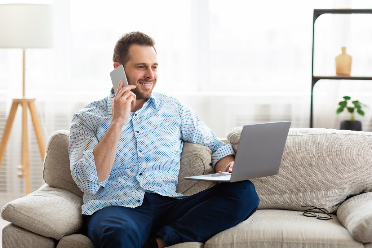 Homme dans son canapé, avec smartphone et PC portable, sourit car content du Wi-Fi 6E sur sa Box Internet