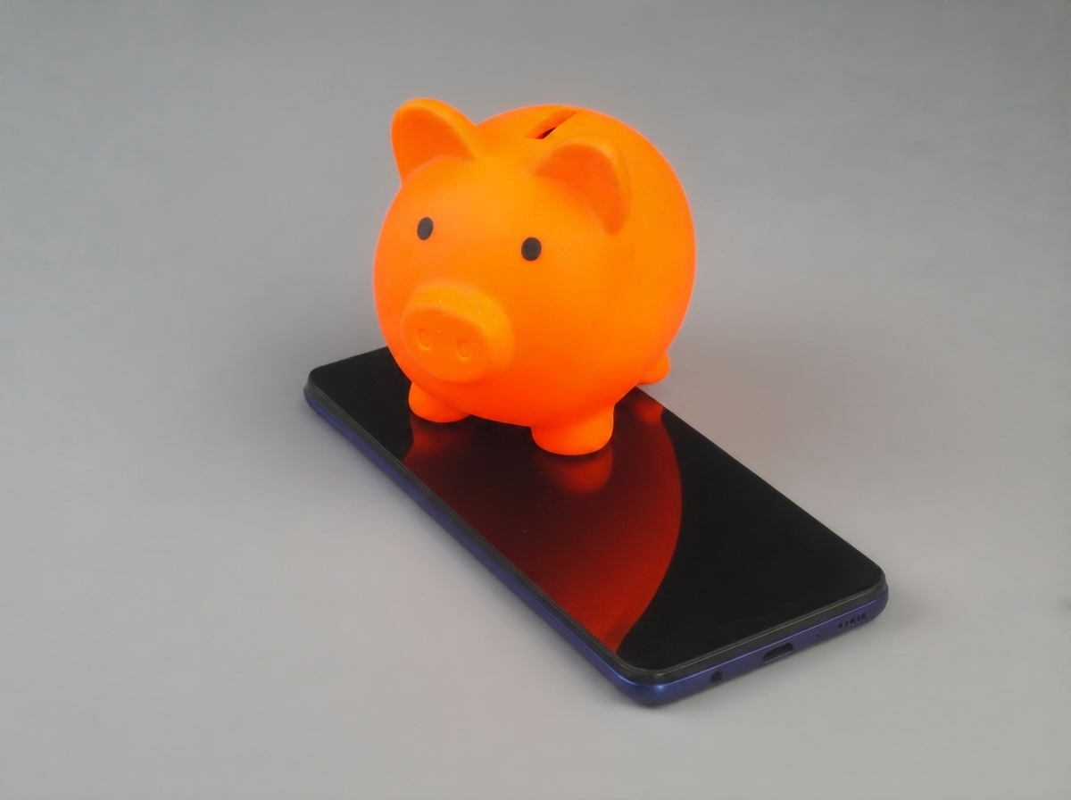 Tirelire cochon de couleur orange posée sur un smartphone, car YouPrice est moins cher que l'opérateur historique Orange